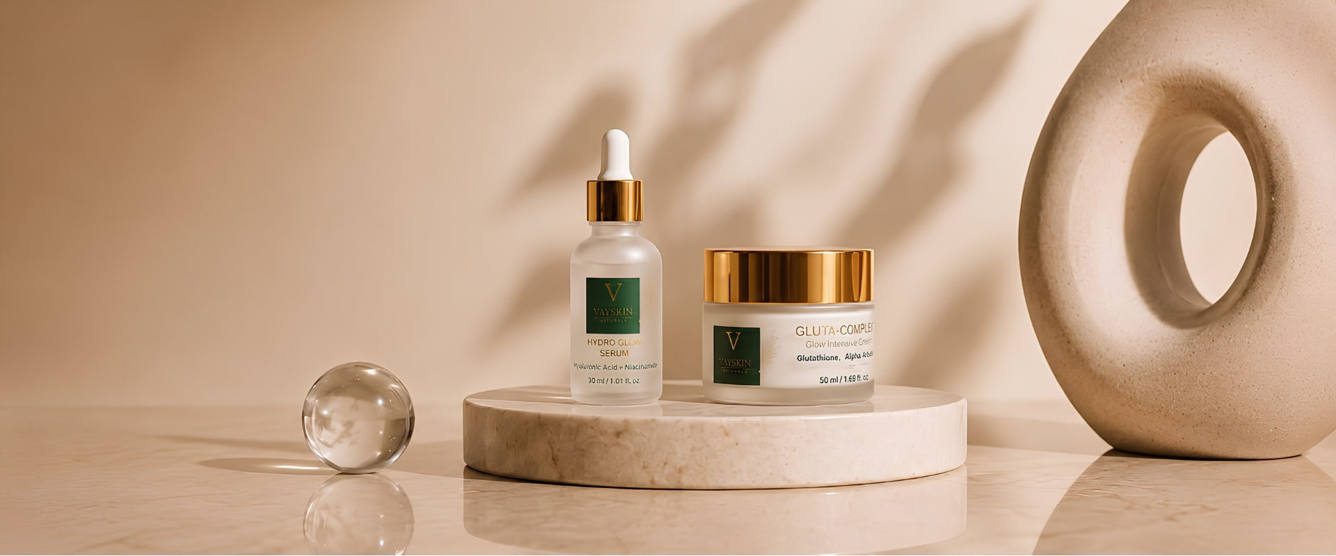 Vové Skin hydrating serum and gluta cream jar displayed on a marble pedestal with a glass sphere